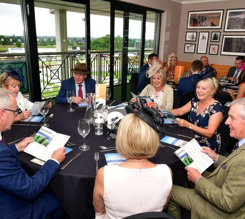 Group of people sitting around a round table, chatting and checking out their race cards.