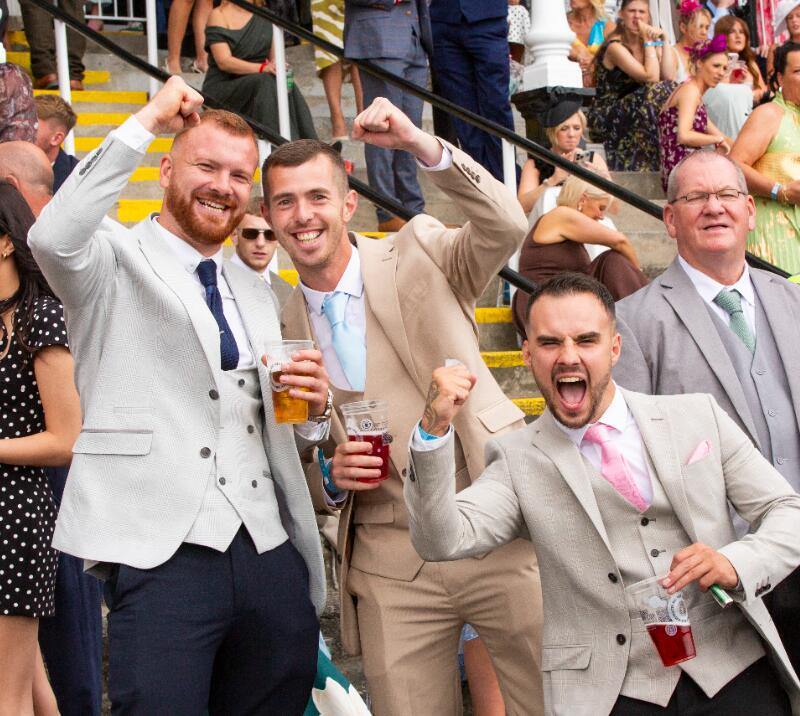 A group of gents in suits at Newcastle Races cheer for the camera