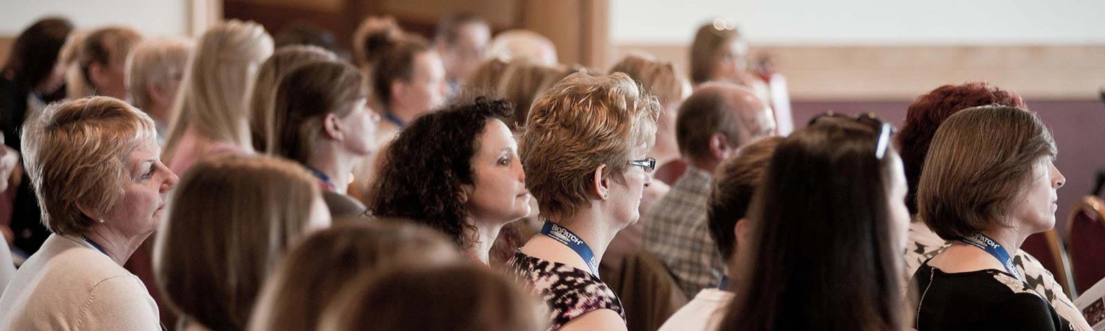 A seated crowd listen to an unseen speaker.