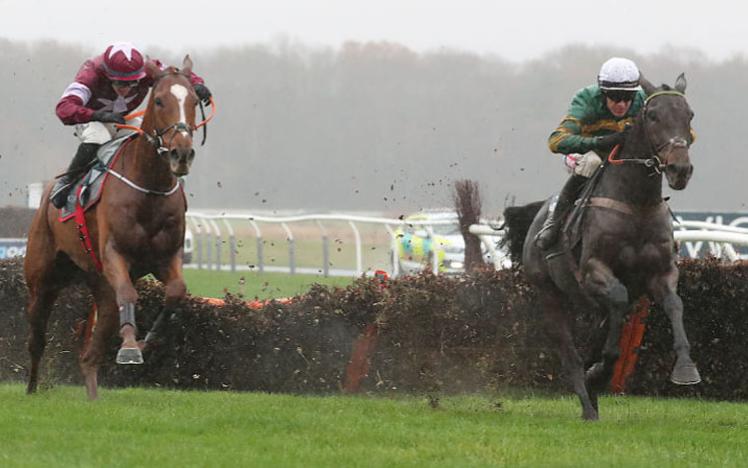 Two horses and jockeys jumping a fence