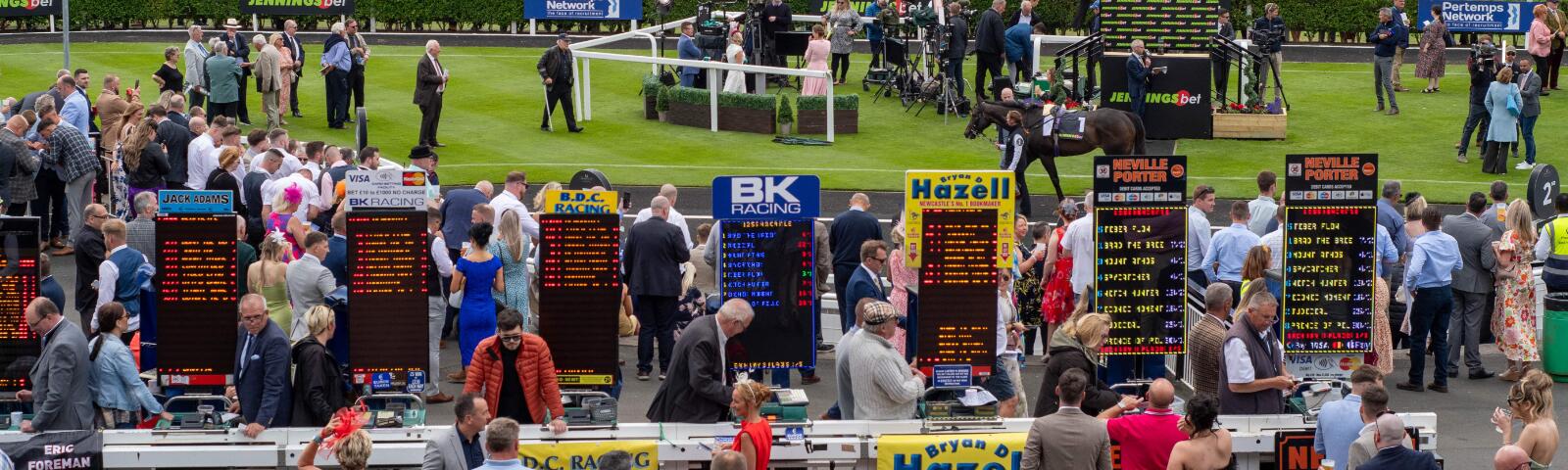 A busy race scene at Newcastle with bookmakers in the front, and the parade ring and interviews in the background